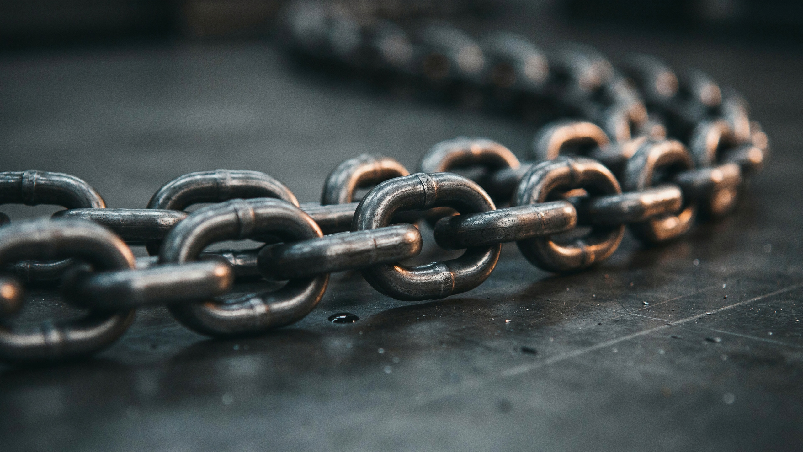 Heavy industrial chain links on dark steel surface, warm amber light, supply chain concept