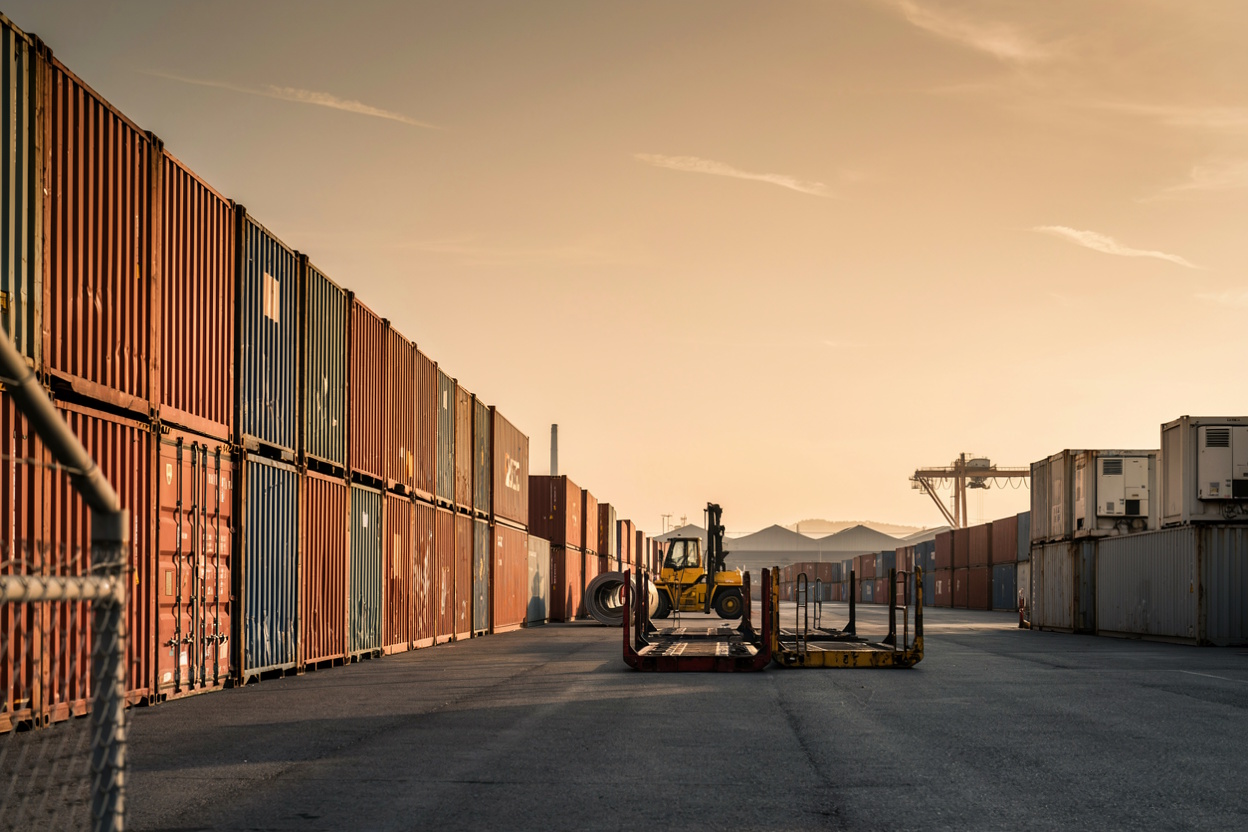 Container yard at golden hour with stacked shipping containers and forklift